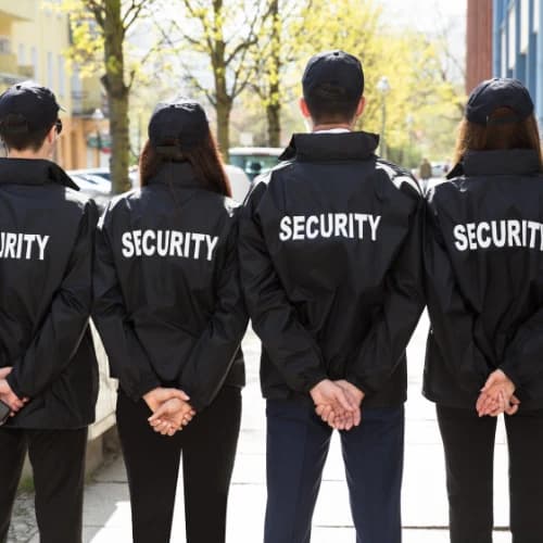 Four security staff in black uniforms standing in a line outside a venue